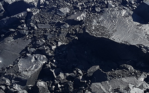 Close-up of a pile of black natural Selenizza bitumen, with a rough surface and shiny flakes.