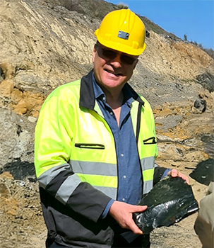 Patrick PASCAL holding a piece of natural Selenizza bitumen on an outdoor mining site.